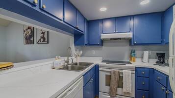 A kitchen with blue cabinets, a white countertop, a sink, a stove, and a coffee maker.