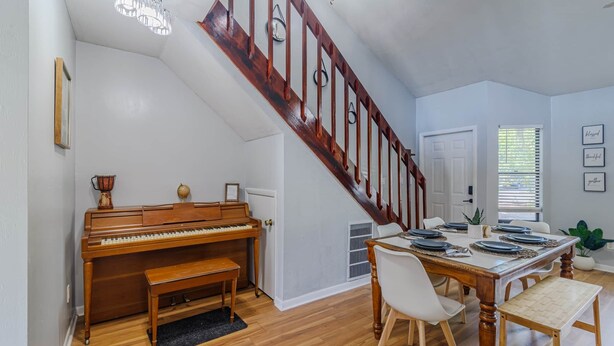 Een eetgedeelte met een houten tafel voor vier personen, een piano en een trap met houten leuning.