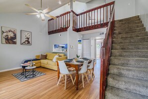 A modern living space with a dining area, a staircase, and a kitchen in the background. - The Modern Gator BBQ House (Gainesville)