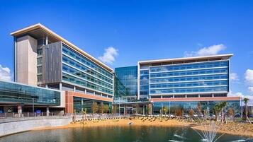 A modern building with a glass facade, a water feature in front, and a clear sky.