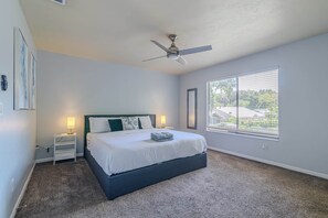 A bedroom with a bed, a ceiling fan, a nightstand, a lamp, and a window with blinds. - The Modern Gator BBQ House (Gainesville)