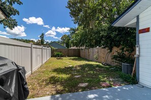 A backyard with a wooden fence, a barbecue grill, and a shed. - The Modern Gator BBQ House (Gainesville)