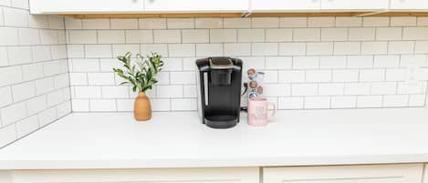 A kitchen with white cabinets, a coffee maker, a plant, and a mug with text.