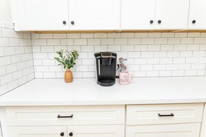 Eine Küche mit weißen Schränken, einer Kaffeemaschine, einer Pflanze und einer Tasse mit Aufdruck.