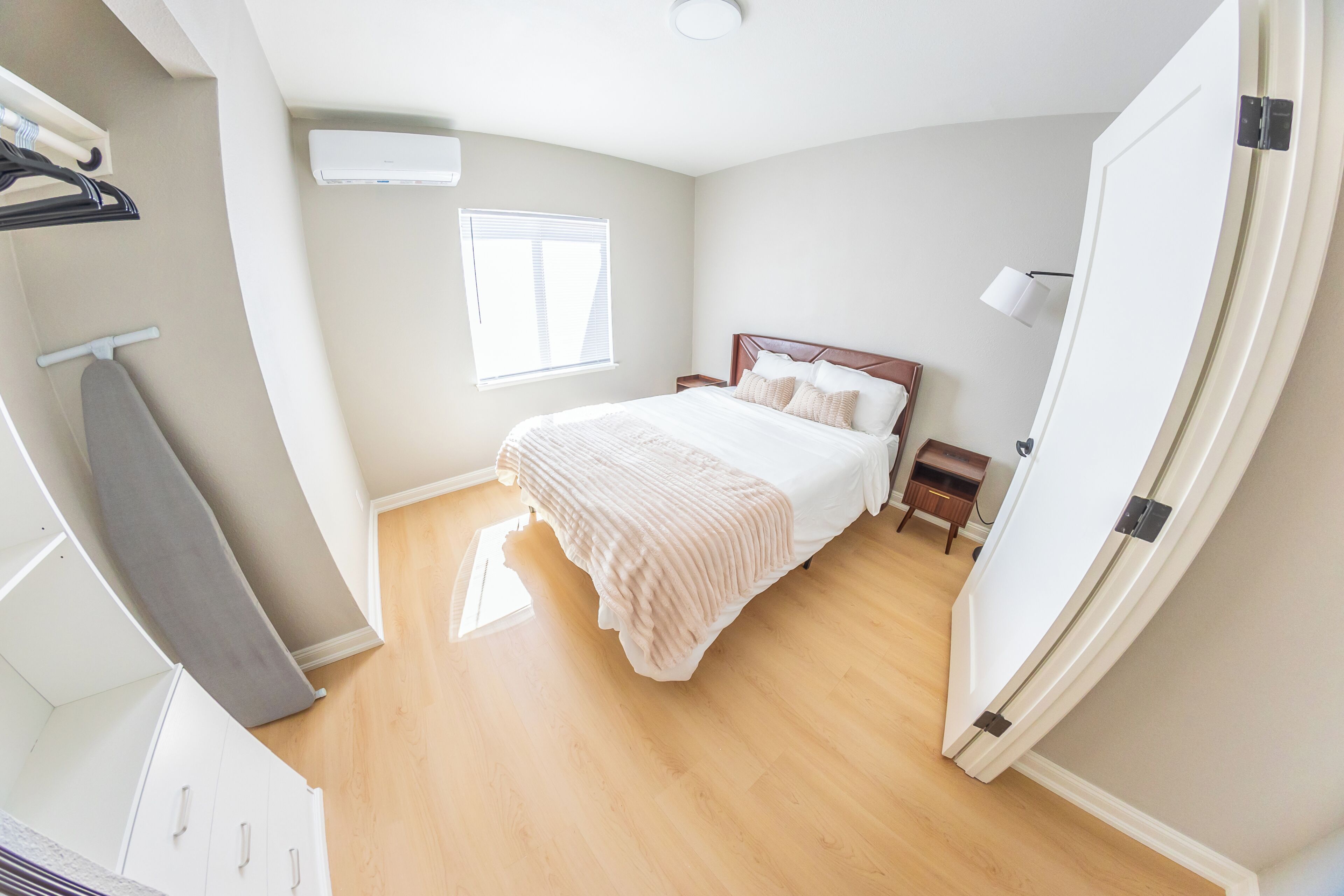A bedroom with a bed, a wardrobe, a window, and an air conditioning unit.