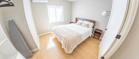 A bedroom with a bed, a wardrobe, a window, and an air conditioning unit.