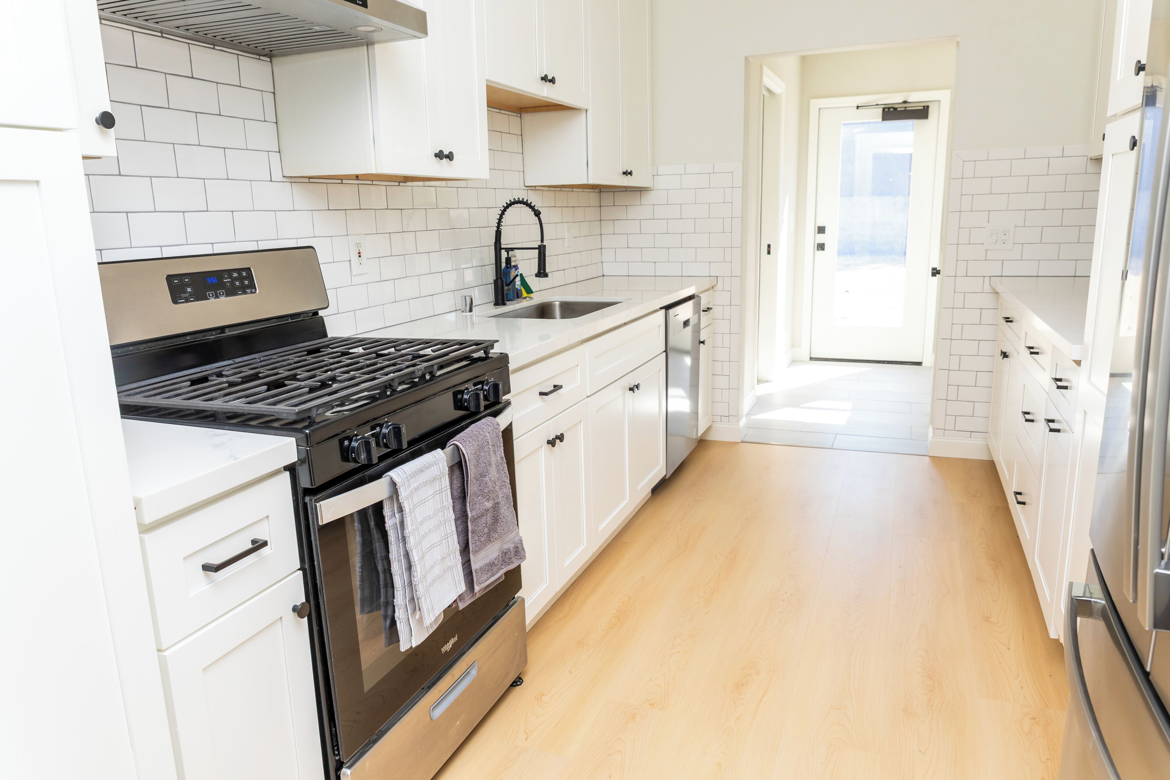 A modern kitchen with white cabinets, a stainless steel stove, and a wooden floor.