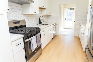 Une cuisine moderne avec des armoires blanches, une cuisinière en acier inoxydable et un plancher en bois.
