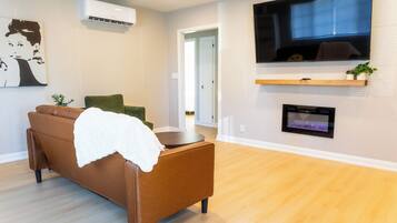 A modern living room with a brown sofa, a flat-screen TV mounted on the wall, and a fireplace below it.