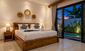 Quarto com cama de madeira, mesa de cabeceira com luminária e vista para uma piscina e plantas através de uma porta de vidro.