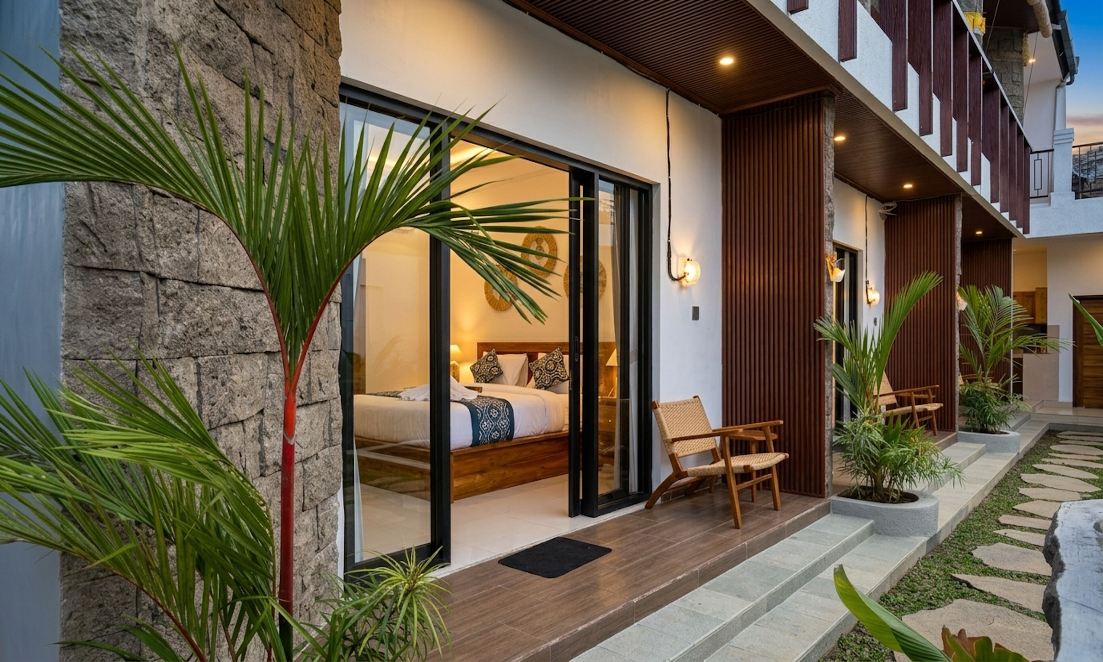Een modern hotel met een gevel van natuursteen, een glazen toegangsdeur, een houten terras en buiten zitplaatsen.