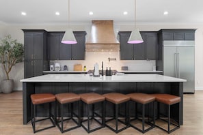 Una cucina moderna con un'isola grande, mobili scuri e illuminazione a sospensione.