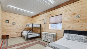 Camera da letto in una baita di legno con letti a castello, una cassettiera e un letto grande.