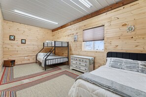 Quarto de cabana de madeira com beliches, cómoda e uma cama grande.