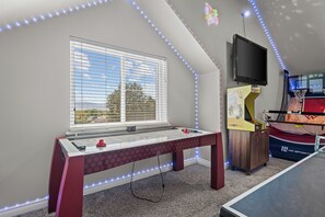 Een kamer met een tafelvoetbaltafel, een televisie en een raam met zonwering.