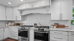 A kitchen with white cabinetry, two stainless steel stoves, and a white tiled backsplash.