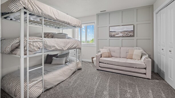 A room with bunk beds, a sofa, a framed picture on the wall, and a window with blinds.