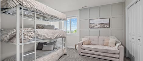 A room with bunk beds, a sofa, a framed picture on the wall, and a window with blinds.