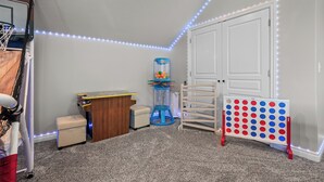 A child's playroom with a basketball hoop, a toy car, a toy kitchen set, a toy basketball hoop, and a pegboard with colorful pegs.