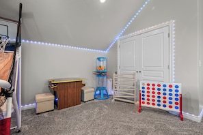 Een kinderkamer met een basketbalring, een speelauto, een keukentje en een prikbord met kleurrijke houten poppen.