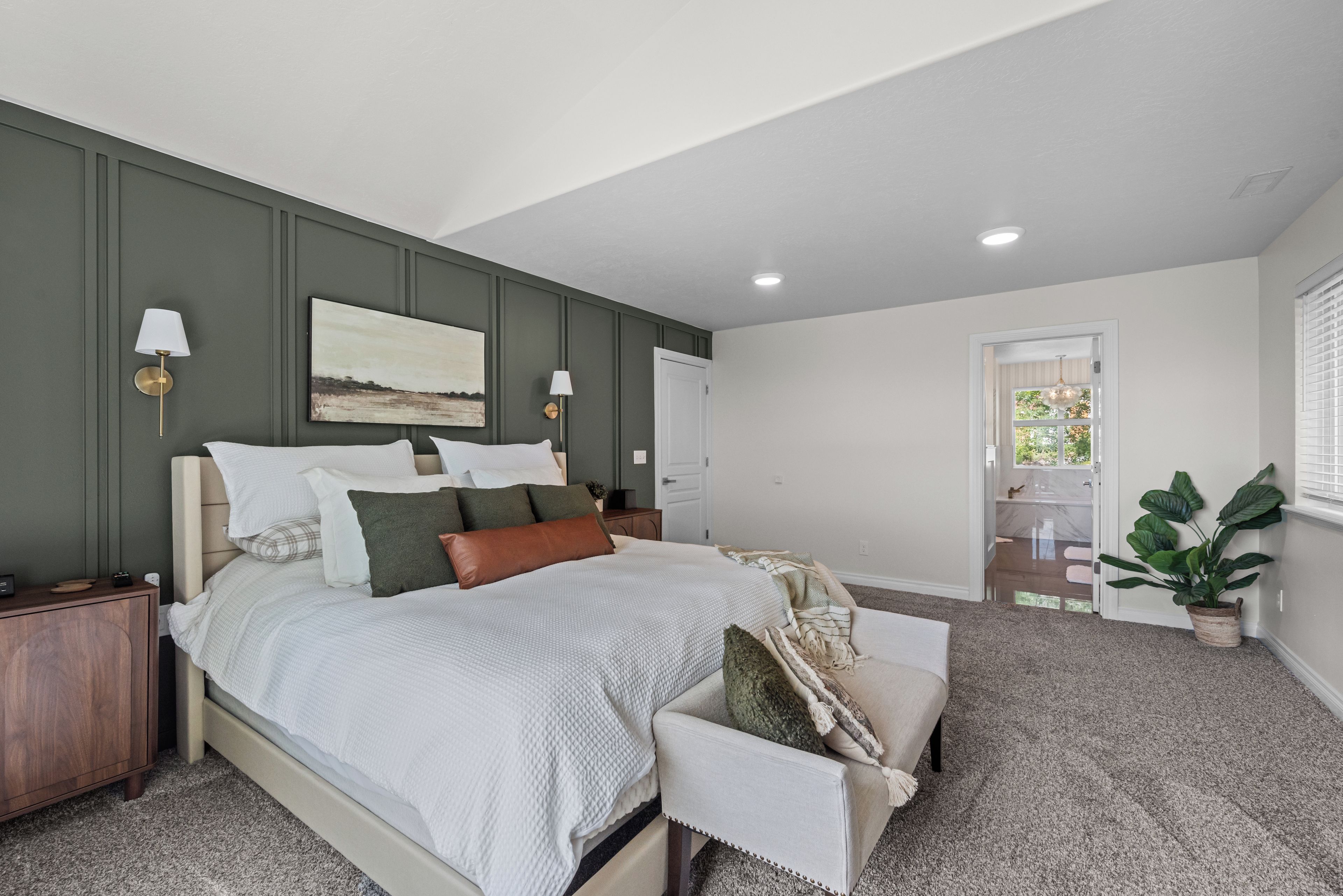 A bedroom with a large bed, bedside lamps, a painting, and a view of the bathroom.