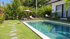 Ein rechteckiger Pool mit einer umlaufenden Sonnenterrasse, einigen Liegestühlen und einem kleinen Sonnenschirm.