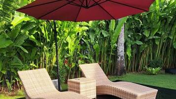 A deck with two lounge chairs and a red umbrella.