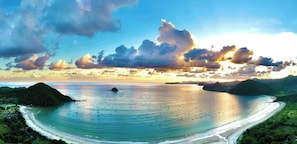 A coastal landscape with a curved shoreline, a small island, and a clear sky with clouds.
