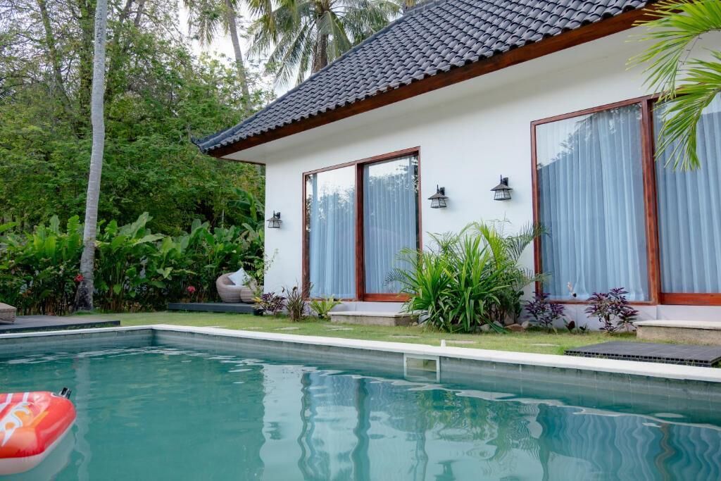 Piscina com deck revestido, rodeada por vegetação exuberante e uma casa moderna com janelas amplas e telhado em cerâmica.