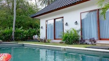 Piscina com deck revestido, rodeada por vegetação exuberante e uma casa moderna com janelas amplas e telhado em cerâmica.