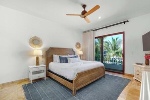 A bedroom with a wooden bed, two bedside tables with lamps, a ceiling fan, and a view of palm trees through a sliding glass door. - 5 BR Villa + Private Pickleball & Pool +Views (Cabo San Lucas)