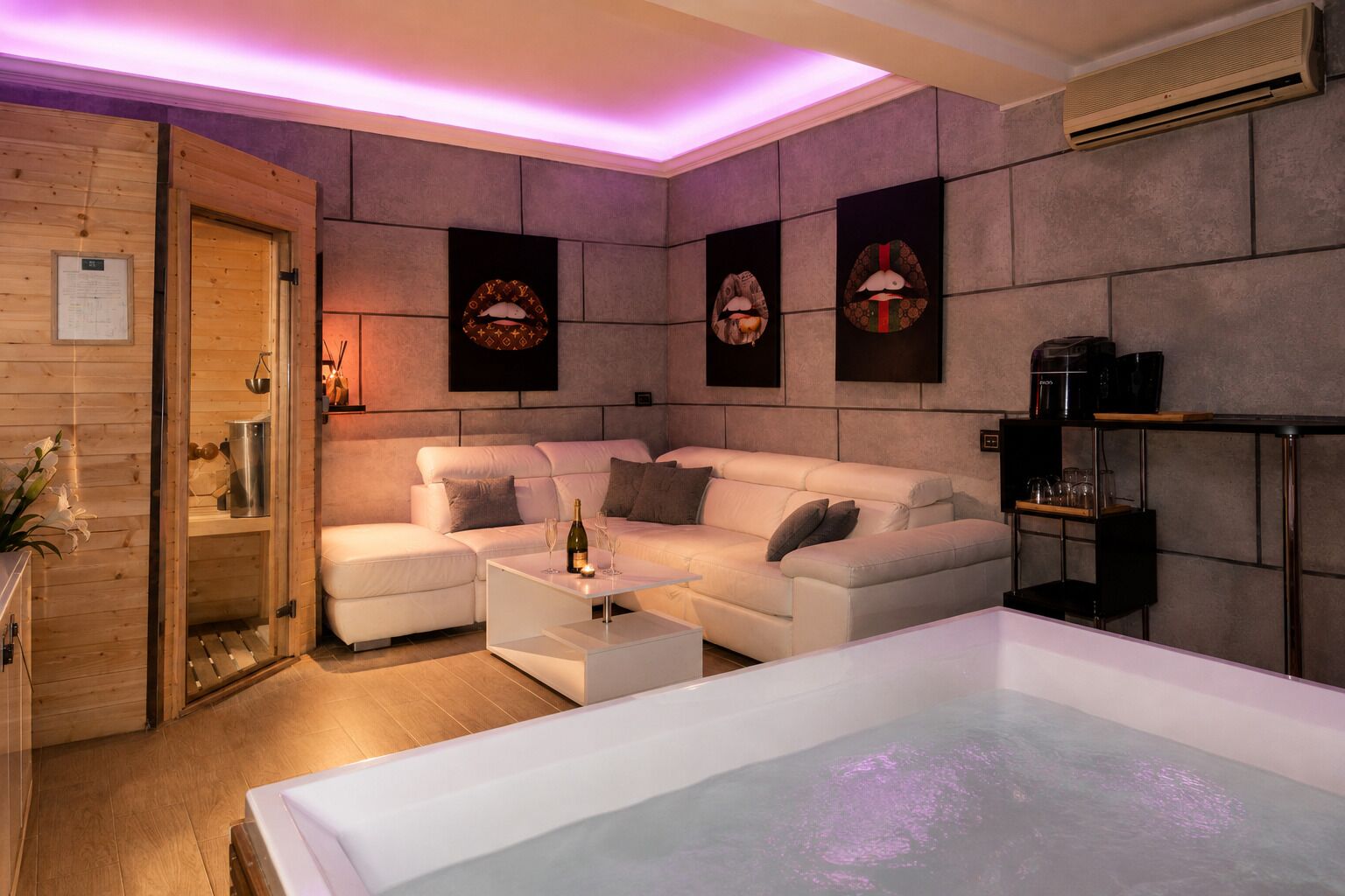 A modern spa room with a white sofa, a massage table, and a coffee machine.