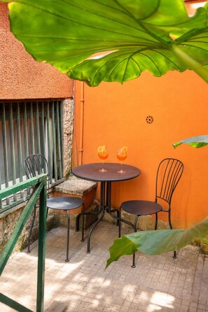 An outdoor seating area with a round table and two chairs, two glasses of a beverage, and a large green plant. - The Spa Suite City Relax By RHR (ROMA)