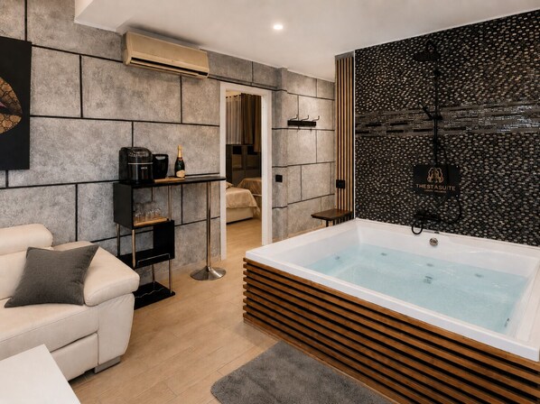 Un baño moderno con una bañera grande, zona de ducha y área de descanso con sofá y cafetera.