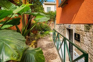 A courtyard with a stone wall, a green metal railing, and lush greenery. - The Spa Suite City Relax By RHR (ROMA)