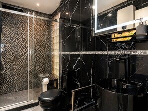 Un baño moderno con pared de mármol negro, cabina de ducha de vidrio y inodoro negro.