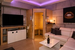 A modern living room with a flat-screen TV, a sofa, a coffee table with a bottle and glasses, and a sauna door. - The Spa Suite City Relax By RHR (ROMA)