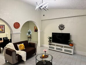 A living room with a sofa, TV, and decorative plants.