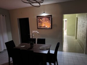 Un comedor con una mesa, sillas, un jarrón con flores y un cuadro en la pared.