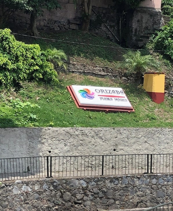 A sign for 'ORIZABa Pueblo Médico' in a grassy area with a stone wall and vegetation in the background.