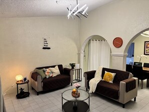 Una sala de estar con dos sofás, una mesa de centro, un reloj de pared y un letrero decorativo.