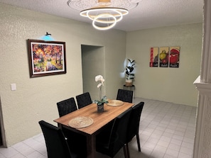 A dining area with a wooden table, black chairs, a decorative ceiling light, and wall art.
