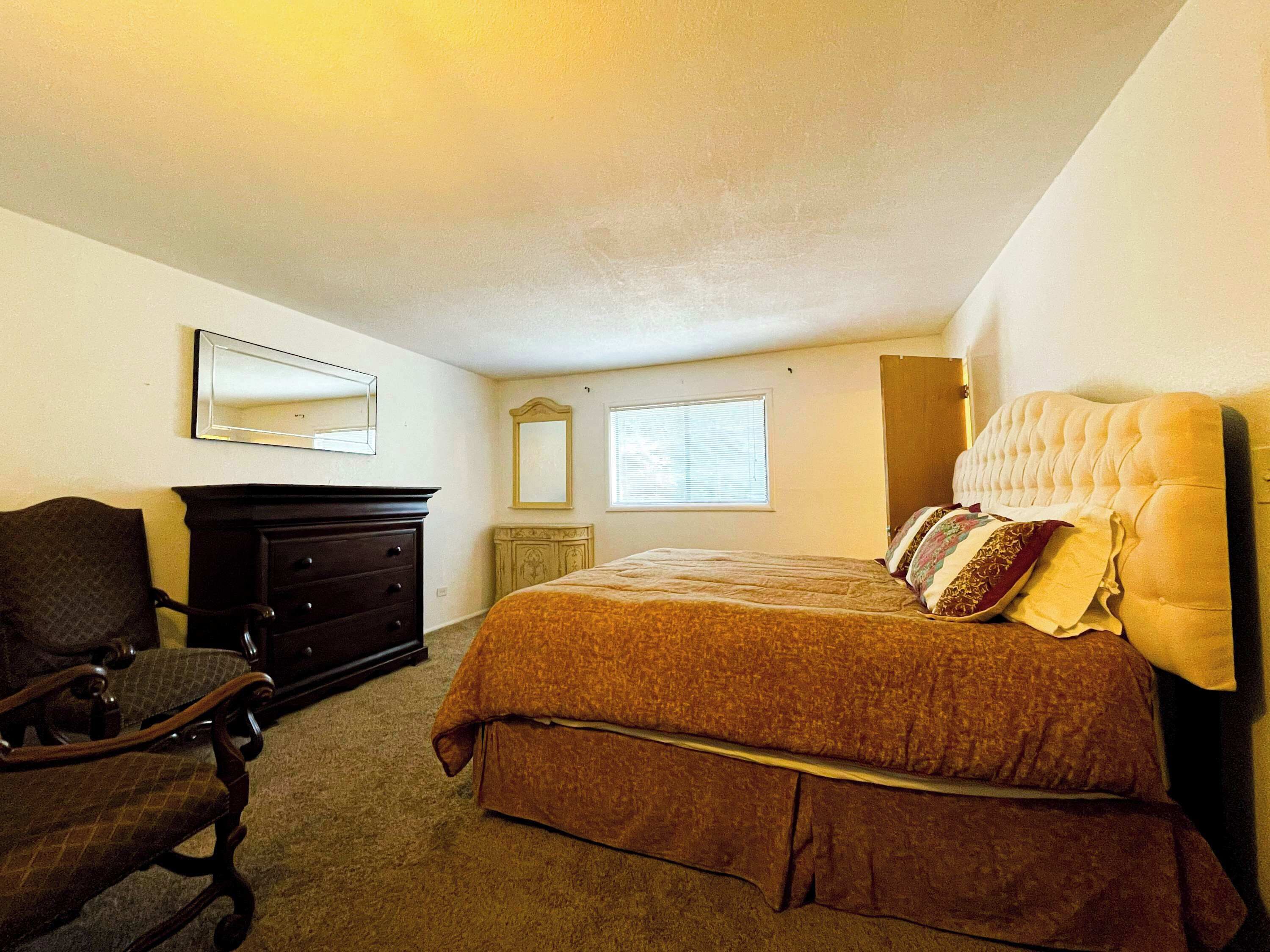 Un dormitorio con cama, cómoda, silla y dos espejos.