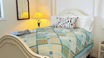Una cama bien hecha con un edredón estampado, una lámpara de noche y un espejo en la pared.