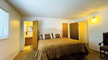 Une chambre à coucher avec un grand lit, une chaise, une armoire et une salle de bain visible à travers une porte ouverte.