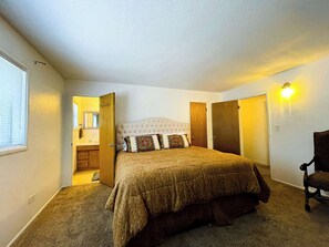 A bedroom with a large bed, a chair, a wardrobe, and a bathroom visible through an open door. - Legacy Homestead Cabin, White Mountains AZ (Navajo County)