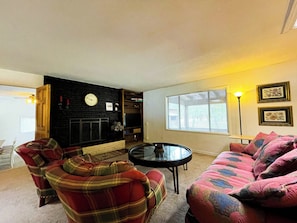 A living room with a fireplace, a sofa, a plaid armchair, a coffee table, and a television. - Legacy Homestead Cabin, White Mountains AZ (Navajo County)