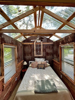 A cozy cabin room with a bed, a wooden ceiling, and a window with blinds. - Unique Treehouse - tiny home combo accommodation in the Ozarks under the stars! (Patterson)