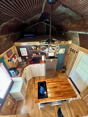 A compact kitchen with a wooden countertop, a built-in stove, and a hanging light fixture. - Unique Treehouse - tiny home combo accommodation in the Ozarks under the stars! (Patterson)