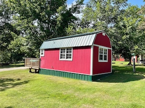 A red wooden structure with a green base, a metal roof, and a wooden deck. - Unique Treehouse - tiny home combo accommodation in the Ozarks under the stars! (Patterson)